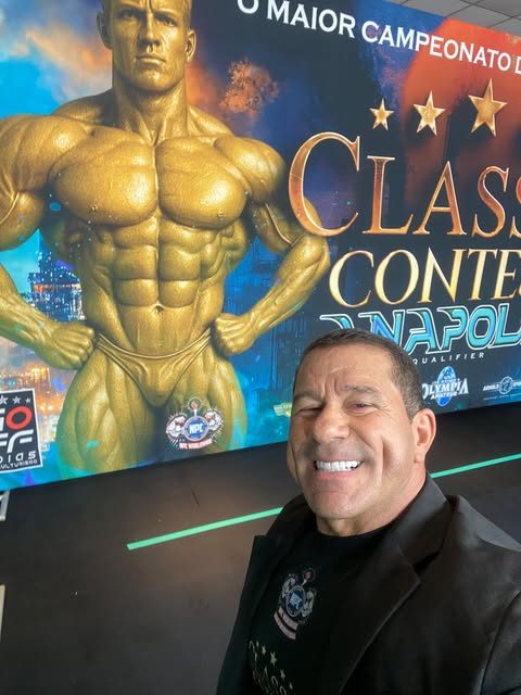 Agostinho Figueiredo, o Katão, sorrindo em frente ao painel de um campeonato de fisiculturismo
